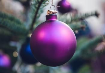 A purple Christmas ball hangs from a tree.